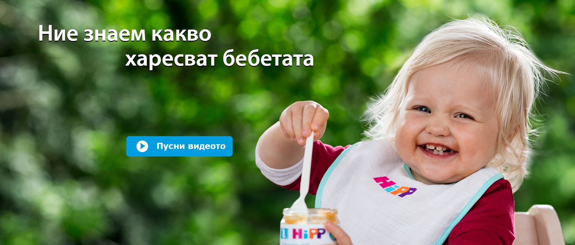 Малко дете с руса коса яде от буркан с лъжица на зелен фон на открито.