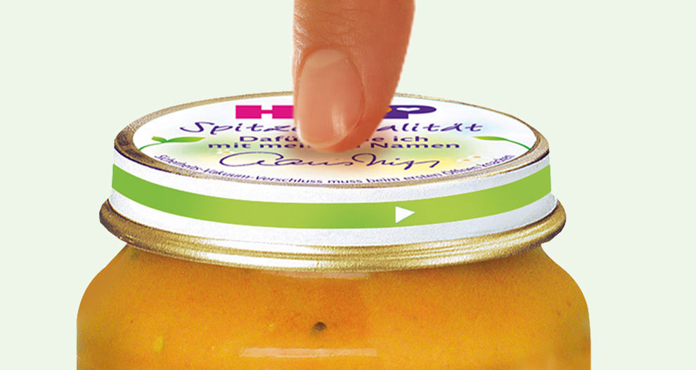 Една ръка се кани да отвори буркан с оранжев хранителен продукт със зелен капак.