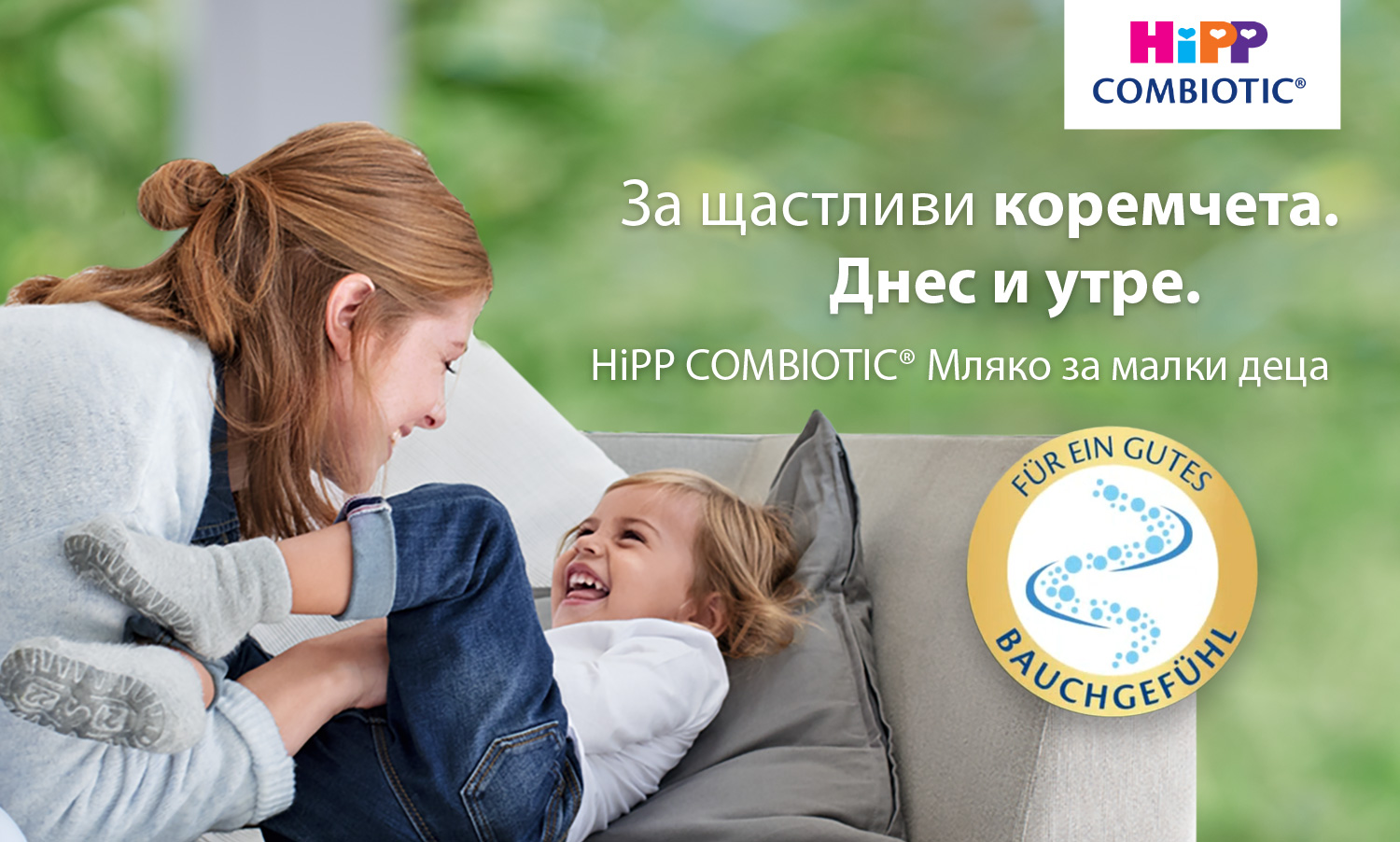 Жена и смеещо се дете са изобразени на диван, жената държи краката на детето, а в горния десен ъгъл има лого "HiPP COMBIOTIC".