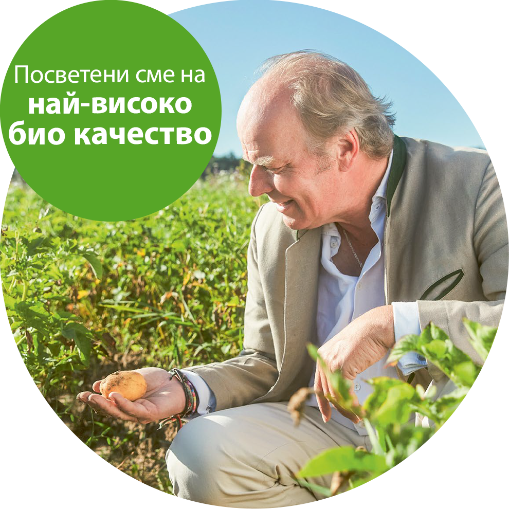 Мъж в бежов костюм е коленичил в полето и държи картоф, а на заден план се вижда зелен балон с бял текст.