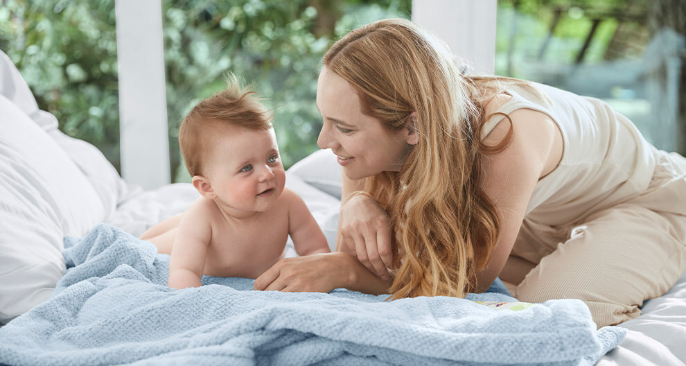 A woman and a baby are lying on a bed, looking at each other.
