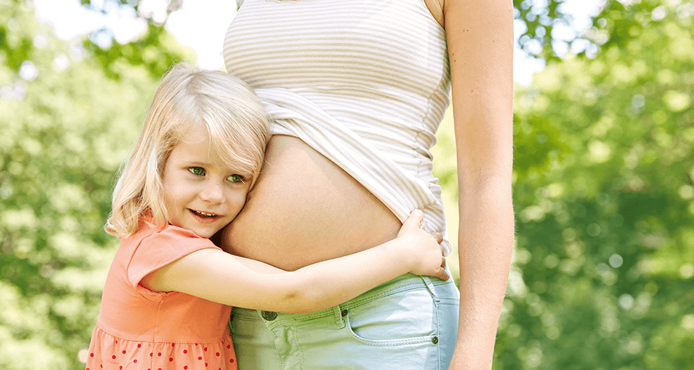 A young girl embraces a pregnant woman outdoors.