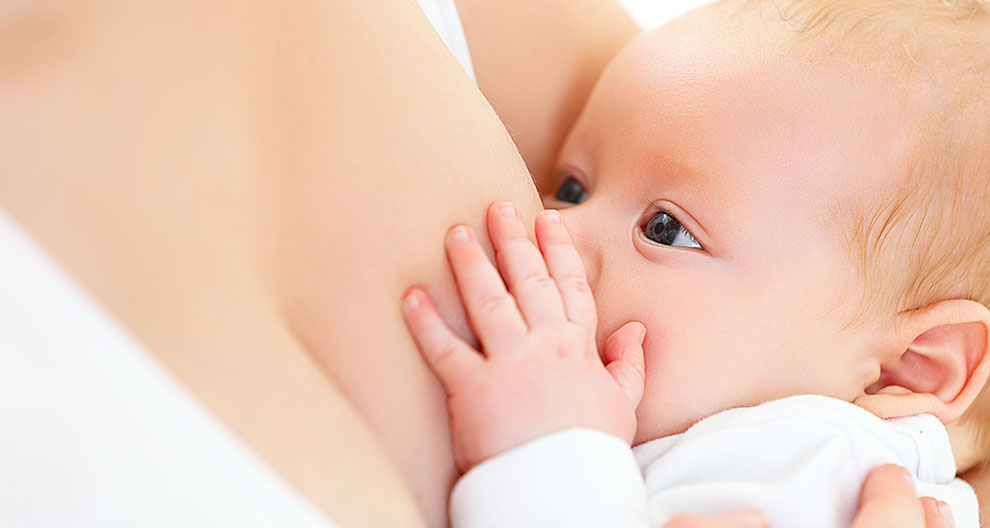 A close-up of a baby's face, with one eye visible, as the baby nurses from a woman's breast.