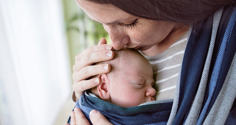 A woman is holding a baby wrapped in a blue cloth.