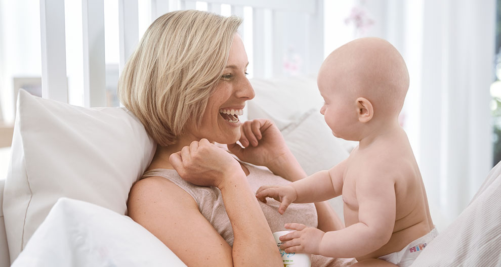 A woman and a baby are lying on a bed, looking at each other.