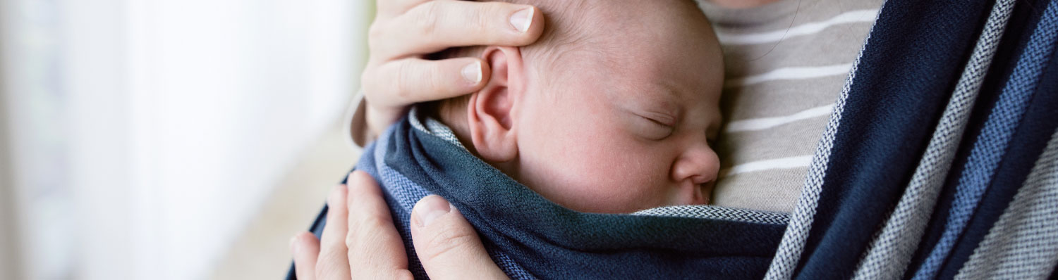 A close-up of a baby's face, partially covered by a blue cloth, cradled by a hand.
