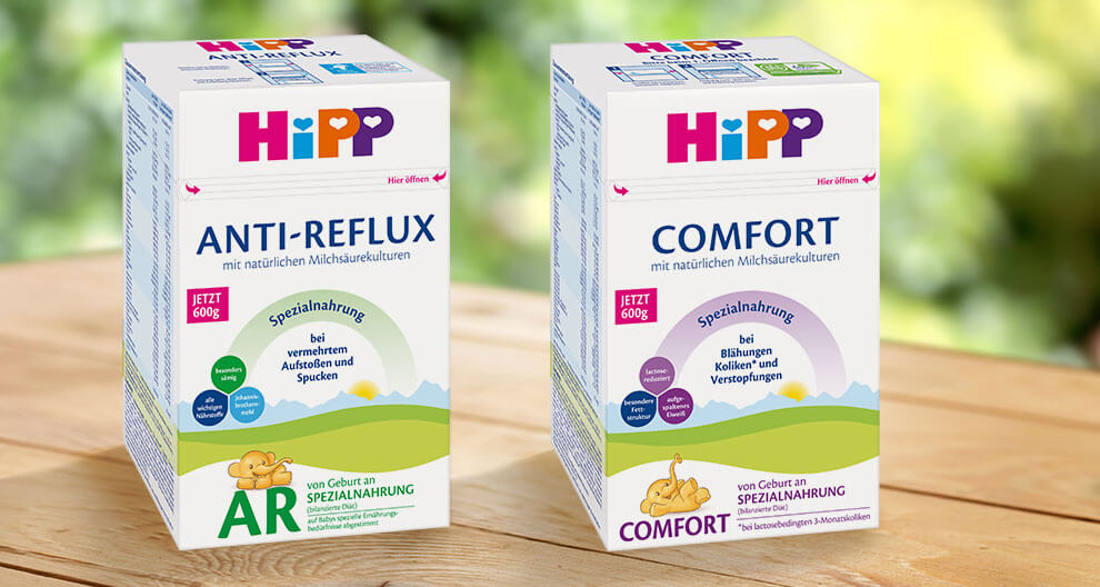 Two boxes of baby products, one labeled "ANTI-REFLUX" and the other "COMFORT," are displayed on a wooden surface with a blurred green background.