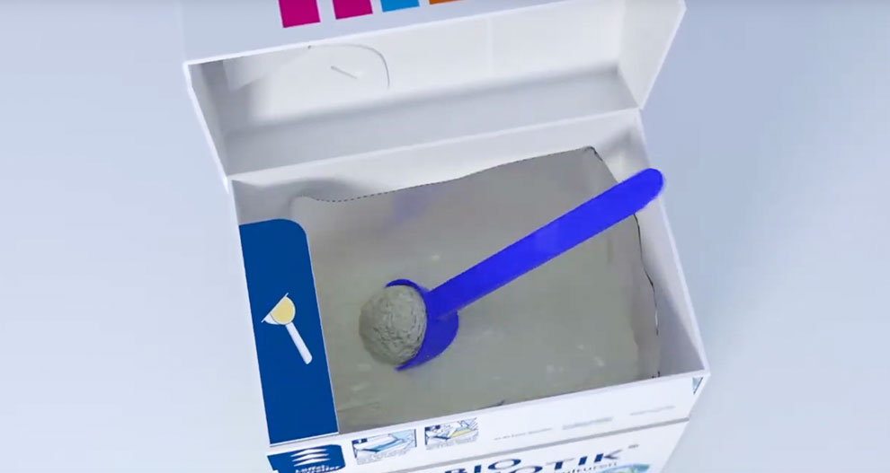 A white box with a blue plastic scoop containing a gray substance.